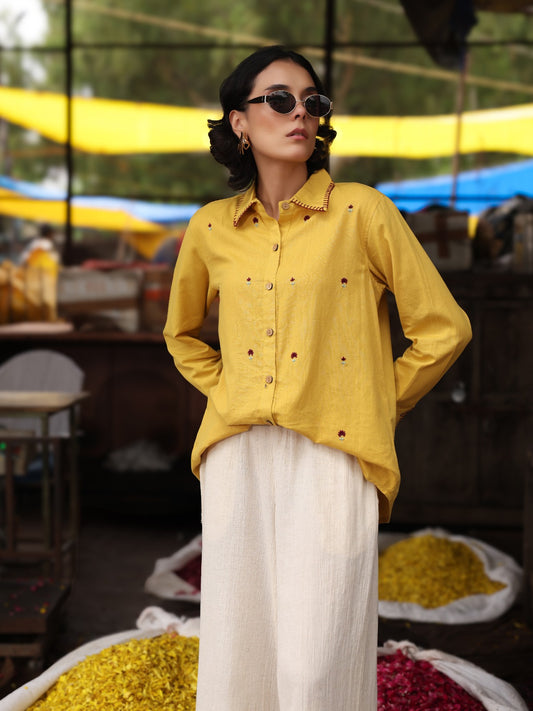 Woman wearing a yellow shirt and sunglasses in an outdoor setting with colorful fabrics.